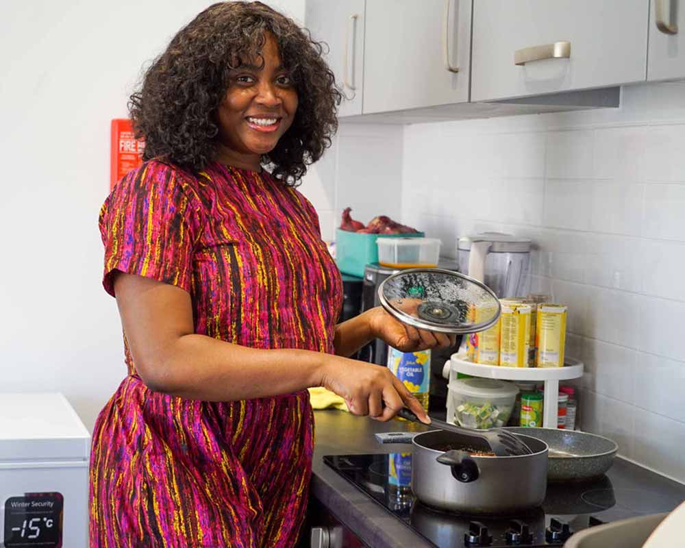 Young lady smiling to camera whilst cooking a meal in her bright and modern YMCA flat.