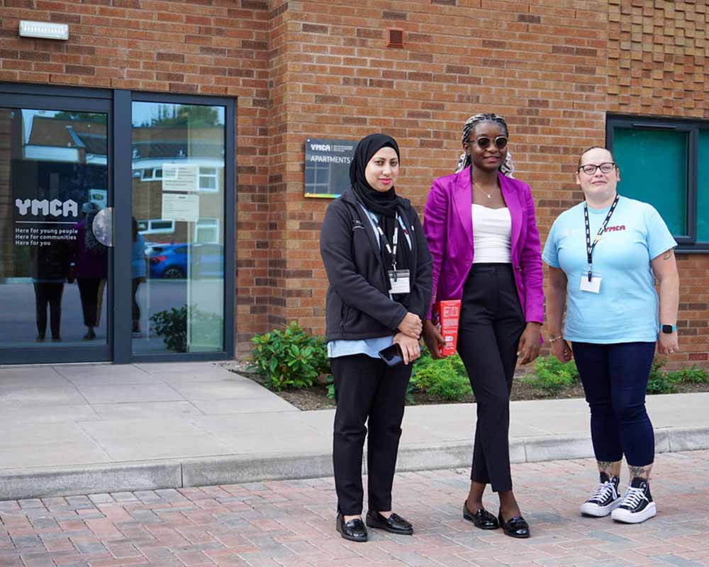 Y-Living staff and resident stood outside new YMCA building smiling to camera