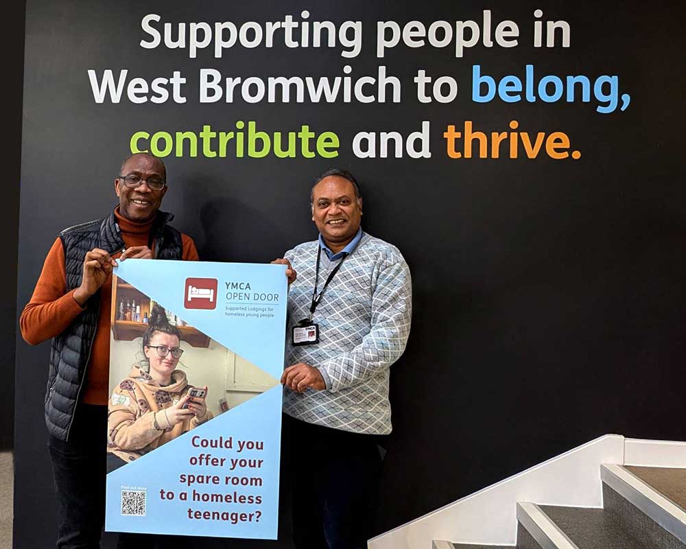 Two men holding up a poster to recruit volunteer hosts to support vulnerable teenagers